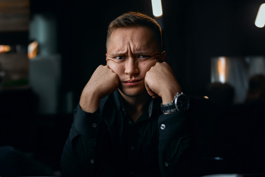 An unhappy caucasian young male with both his fists in his cheeks